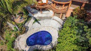 An aerial view of a resort with a swimming pool, a staircase leading to a terrace, and lush greenery.