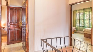 A hallway with a wooden door, a tiled floor, and a view of a bedroom with a bed and curtains. -  Casa Nubes (Puerto Carrillo)