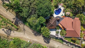 An aerial view of a property with a swimming pool, a tiled roof, and lush greenery.