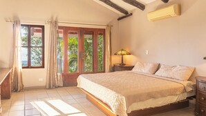 A bedroom with a large bed, a nightstand, a lamp, and a window with curtains. -  Casa Nubes (Puerto Carrillo)