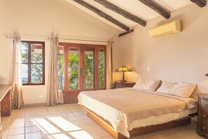 A bedroom with a large bed, a nightstand, a lamp, and a window with curtains. -  Casa Nubes (Puerto Carrillo)