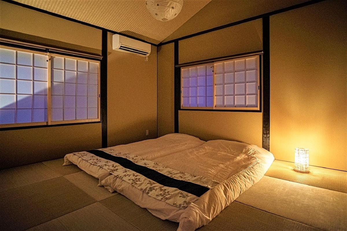 Una habitación tradicional japonesa con suelo de tatami, un futón, puertas correderas shoji y un ventilador de techo.