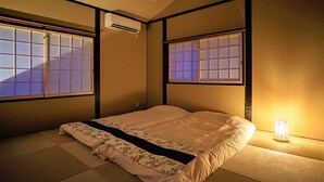 Una habitación tradicional japonesa con suelo de tatami, un futón, puertas correderas shoji y un ventilador de techo.