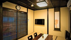 Una habitación tradicional japonesa con suelo de tatami, una mesa baja con un jarrón, un reloj y una obra de arte enmarcada en la pared.