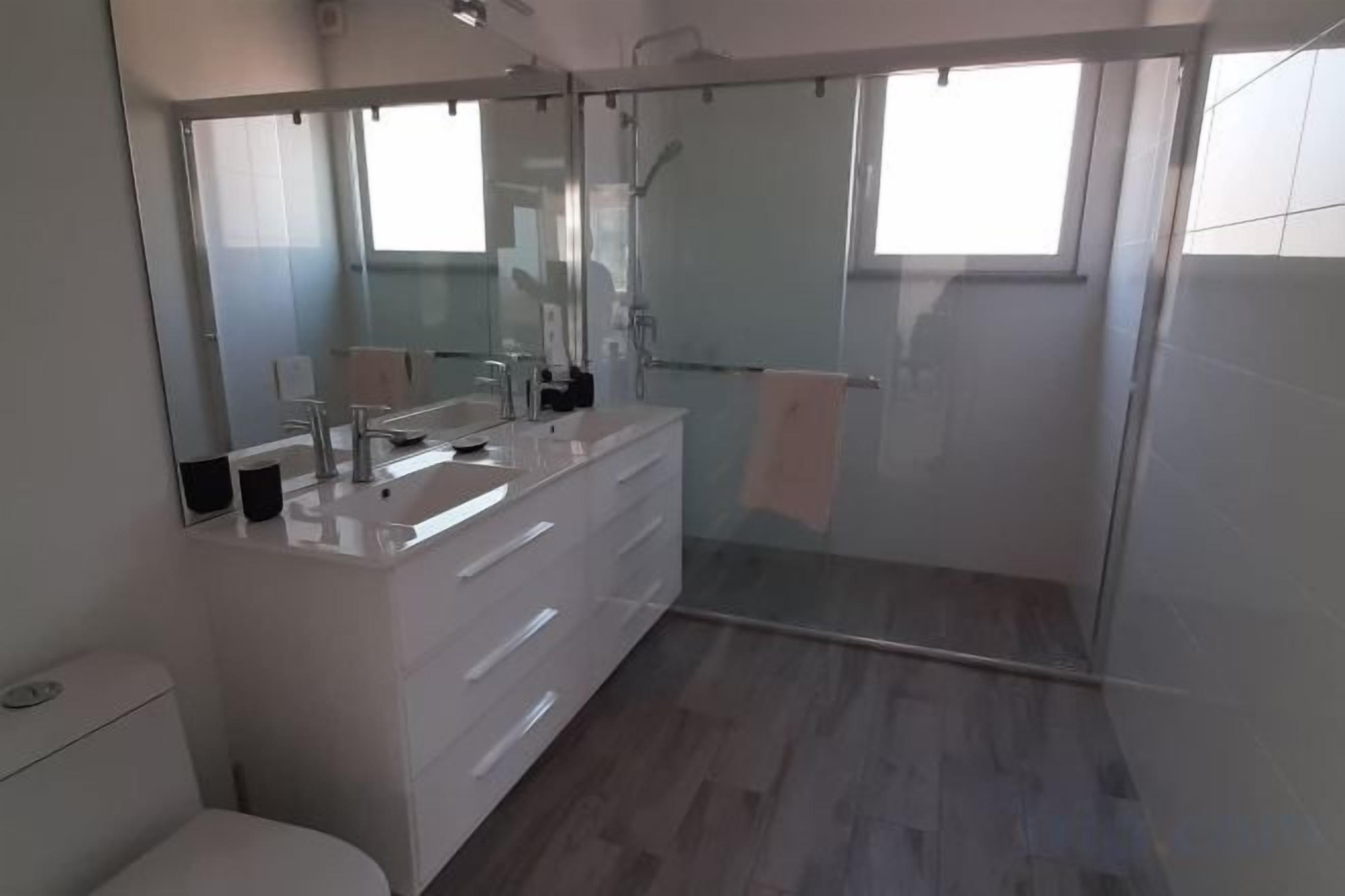 A modern bathroom with a large mirror, a white vanity, and a glass-enclosed shower.