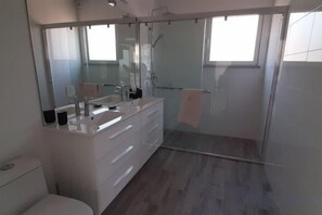 A modern bathroom with a large mirror, a white vanity, and a glass-enclosed shower. - Casa Bananeira (Sao Bartolomeu de Messines)