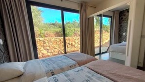 Un dormitorio con una cama grande, vistas al exterior y una pared de piedra.