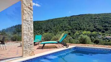 A swimming pool with a stone wall and a view of a forested hill.