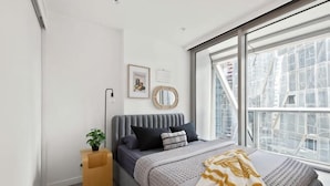A bedroom with a bed, a bedside table, a window, and a wall-mounted mirror. - A Cozy Apt Right Next to Southern Cross Station (Melbourne)