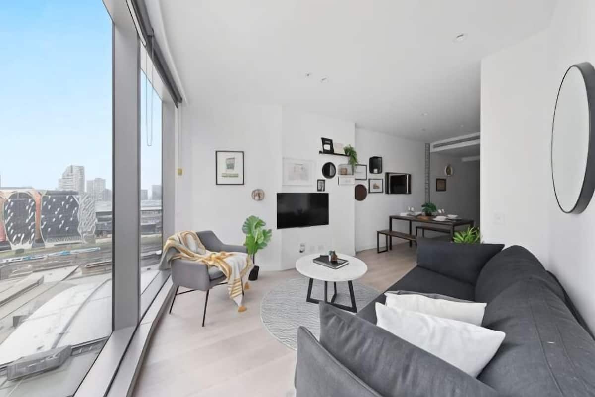 Een moderne woonkamer met een grijze bank, een ronde salontafel en een aan de muur bevestigde televisie.