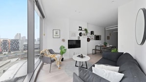 A modern living room with a gray sofa, a round coffee table, and a TV mounted on the wall. - A Cozy Apt Right Next to Southern Cross Station (Melbourne)