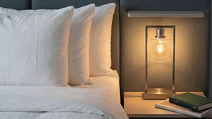 A bed with white linens and pillows, a bedside table with a book and a lamp. - Horizons Sandhills (Patrick)