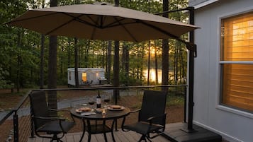 A deck with a table and chairs, an umbrella, and a small house in the background.