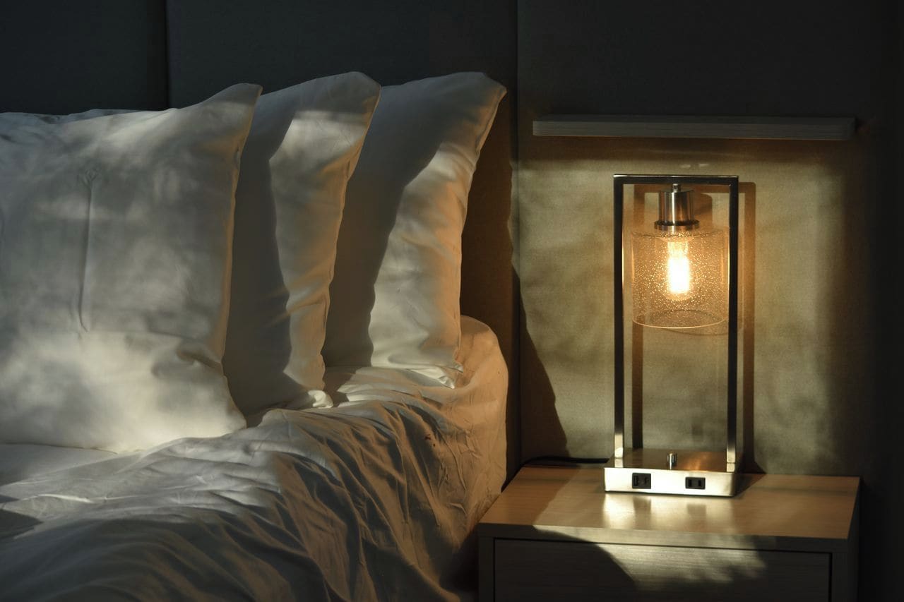 Una cama con sábanas blancas y una mesita de noche con una lámpara.