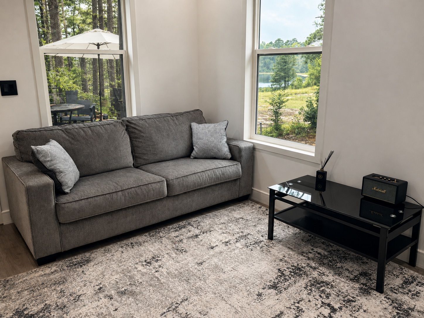 A grey sofa with patterned cushions, a black coffee table, and a view of a green landscape through a window.