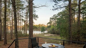 A deck with a table and chairs overlooking a lake, surrounded by trees. - Horizons Sandhills (Patrick)