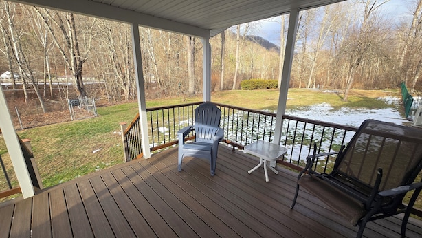 A wooden deck with a chair and table, overlooking a snowy yard and trees.