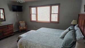 A bedroom with a bed, dresser, chair, and a television mounted on the wall.