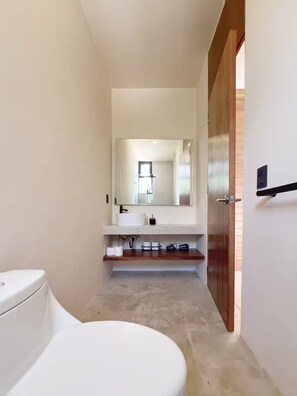A modern bathroom with a white toilet, a sink with a mirror above it, and a wooden door. - PH Cálido con Rooftop + Alberca en Tulum Centro (Tulum)