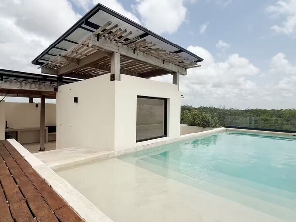 A modern outdoor pool area with a covered seating area and a clear view of the surrounding landscape. - PH Cálido con Rooftop + Alberca en Tulum Centro (Tulum)