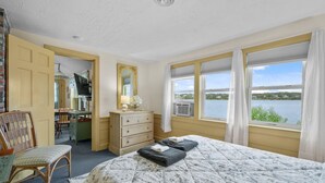 Un dormitorio con cama, cómoda, silla, escritorio, espejo y ventana con vista al lago.