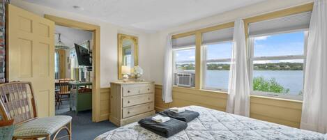 A bedroom with a bed, a dresser, a chair, a desk, a mirror, and a window with a view of a lake.