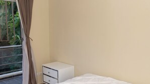 A bedroom with a bed, an air conditioner, a nightstand, and a window with curtains.
