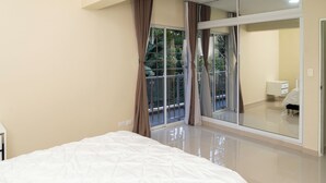 A bedroom with a large bed, a sliding glass door to a balcony, and a small bedside table.