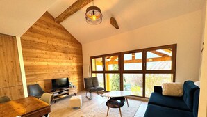 Ein modernes Wohnzimmer mit Holzboden, einem großen Fenster, einer Couch, einem Fernseher und einem Essbereich.