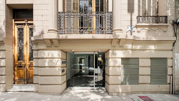 A building entrance with a glass door, a wooden door, and a balcony with metal railings.