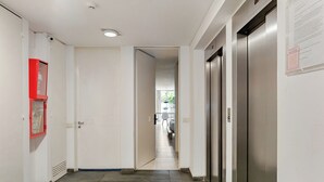 A hallway with a door, a red fire extinguisher, and an elevator.