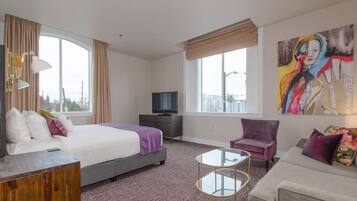 A hotel room with a bed, a TV, a sofa, a chair, and a painting on the wall.