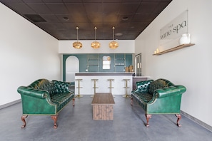 Un área de estar moderna con dos sofás de cuero verde, una mesa de centro de madera y una zona de bar con una pared de acento color turquesa.