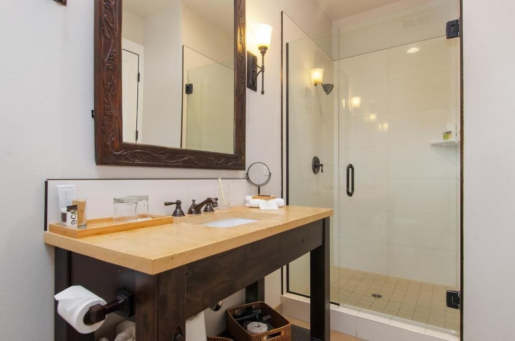 Un baño con tocador de madera, un espejo grande, cabina de ducha de vidrio y un perchero para toallas.
