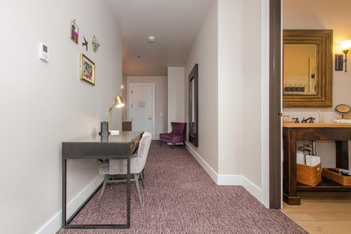 A hallway with a desk, chair, and a purple armchair. There is a mirror and a wooden cabinet with baskets.