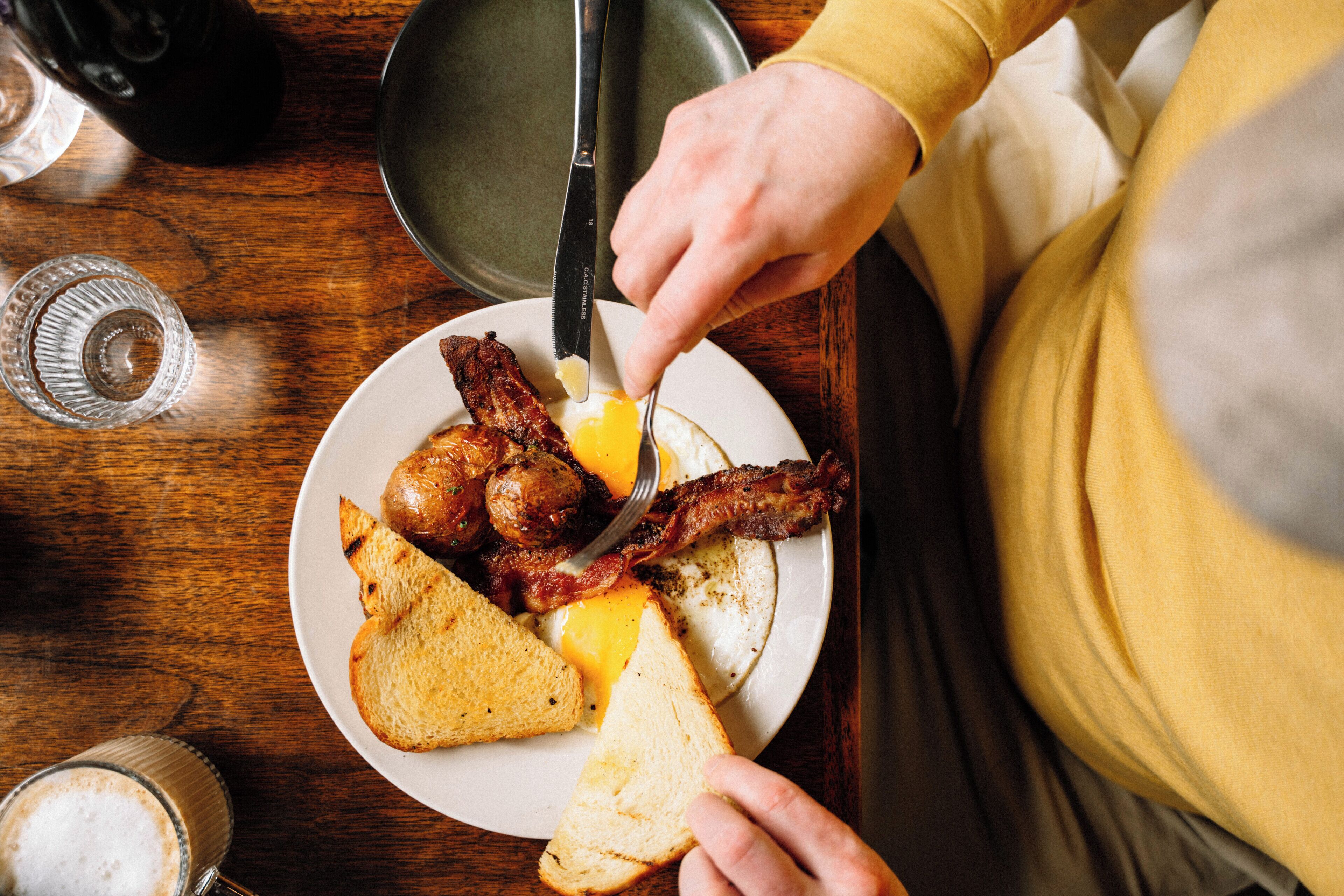 A breakfast plate with bacon, eggs, and toast on a wooden table.