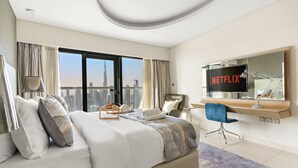 Ein modernes Hotelzimmer mit einem großen Bett, einem Schreibtisch mit einem Laptop, einem Sessel und Blick auf eine Stadtsilhouette.