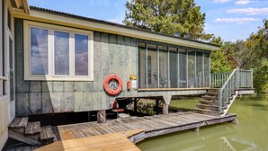 A wooden houseboat with a dock, a lifebuoy, and a staircase leading to a deck.