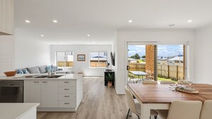 Een moderne keuken met witte kasten, een eethoek met een houten tafel, en een uitzicht op een achtertuin door een glazen deur.