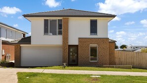 Een tweelaags huis met garage, een bakstenen gevel en een helderblauwe lucht.
