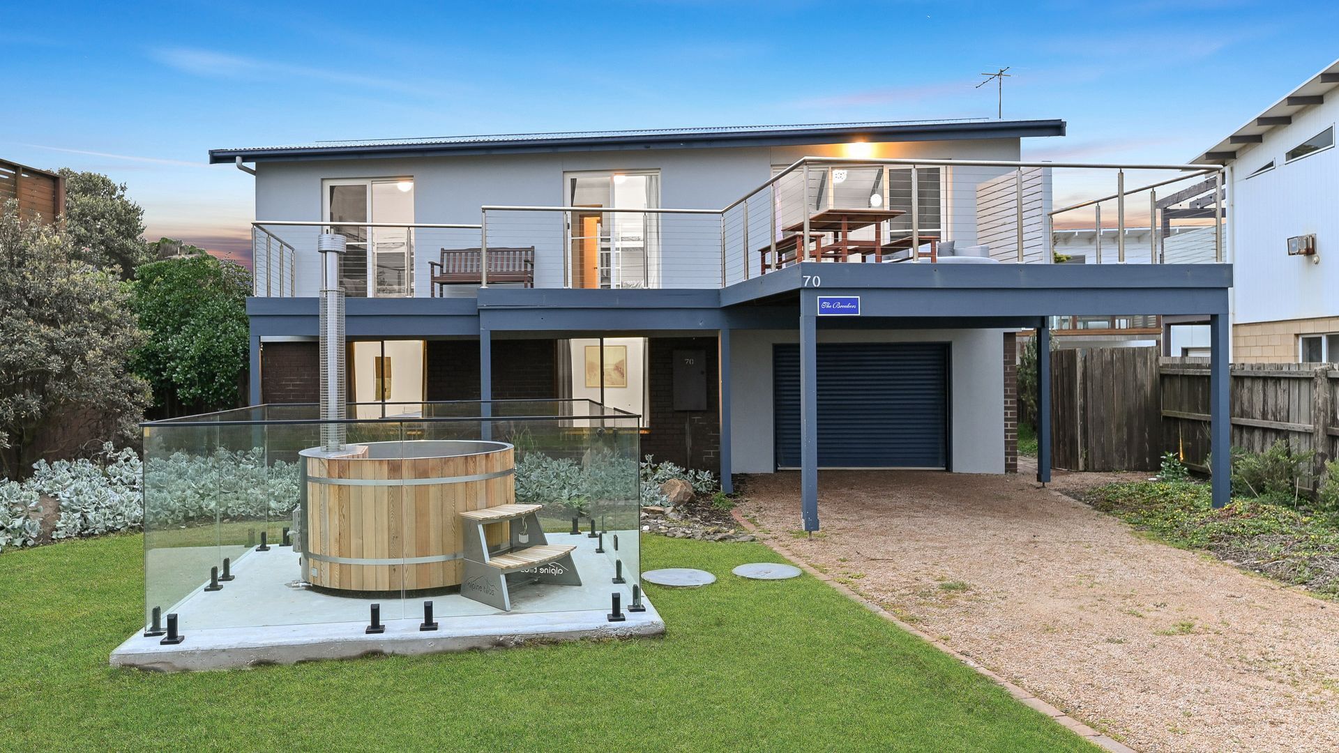 A modern two-story house with a covered patio, a hot tub, and a well-maintained lawn.