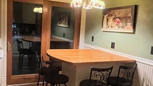 Una cocina con una isla de madera, taburetes de bar, una araña y un cuadro en la pared.