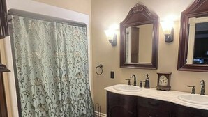 Un baño con inodoro, tocador con lavamanos, dos espejos y cortina de ducha.