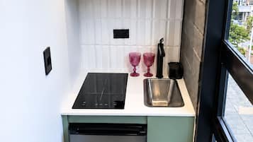 Une petite cuisine équipée avec une cuisinière intégrée, un évier et un lave-vaisselle. On peut voir deux verres roses sur le comptoir, ainsi qu’une machine à café.