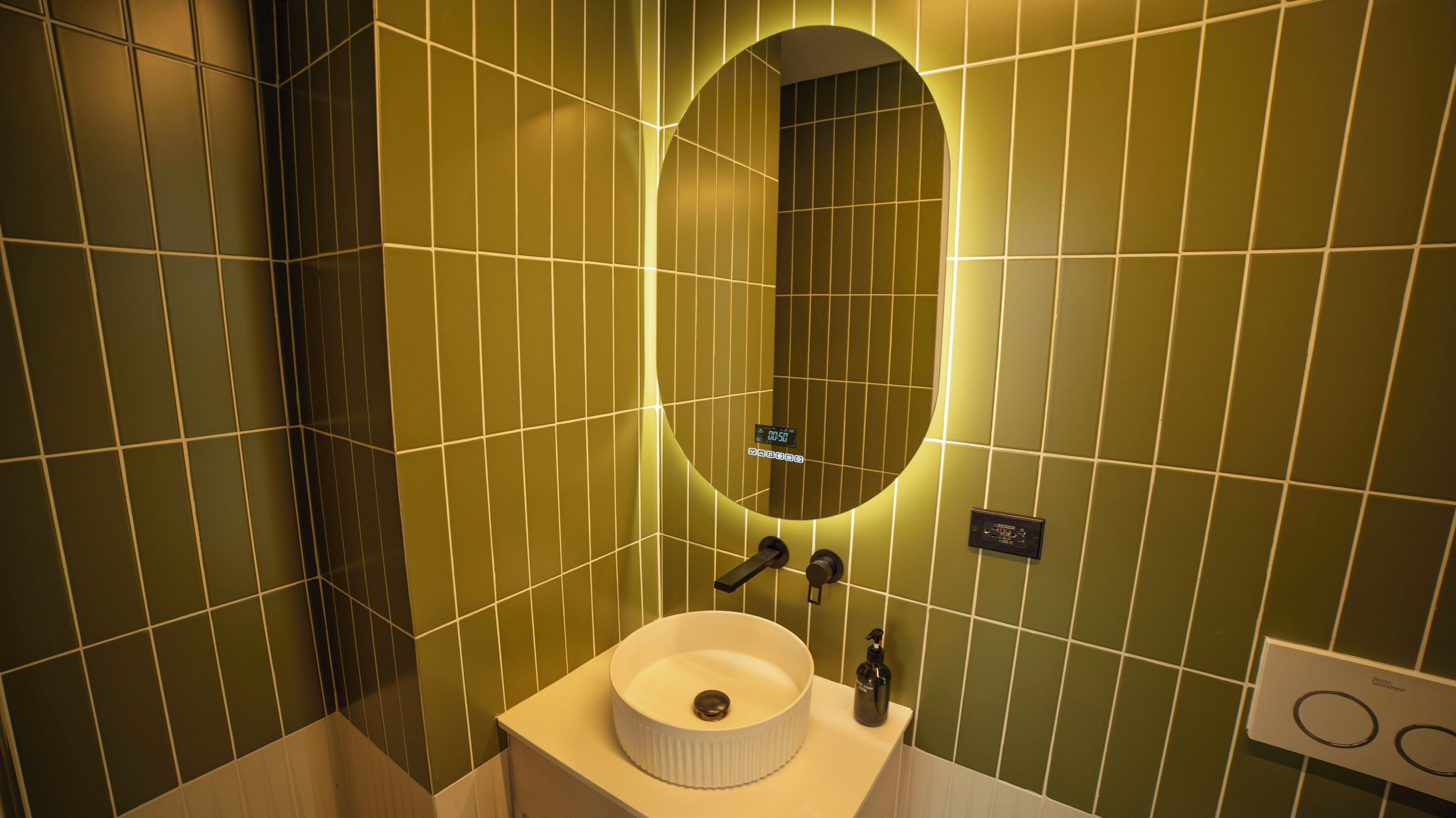 Ein Badezimmer mit einem weißen Waschbecken, einem Spiegel und grünen Fliesenwänden.