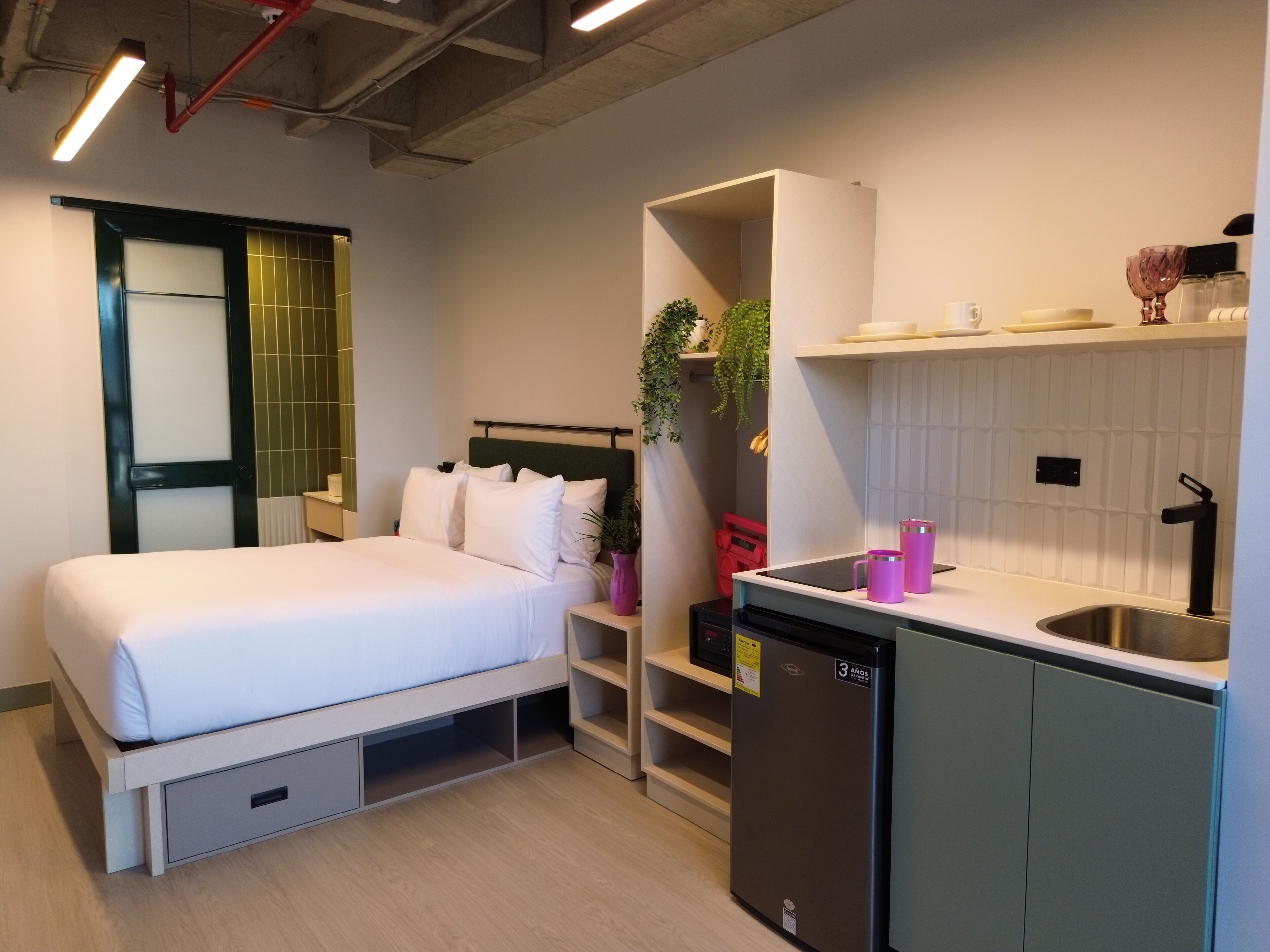 Une chambre d’hôtel compacte comprenant un lit, une petite kitchenette, une étagère intégrée et une fenêtre avec vue.