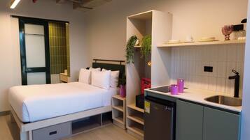 Une chambre d’hôtel compacte comprenant un lit, une petite kitchenette, une étagère intégrée et une fenêtre avec vue.
