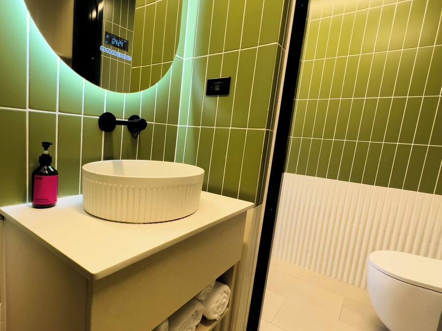 A modern bathroom with a white sink, green-tiled walls, and a white toilet.