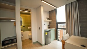 Une chambre d’hôtel moderne dotée d’une kitchenette, d’une salle de bain et d’une grande fenêtre offrant une vue dégagée.