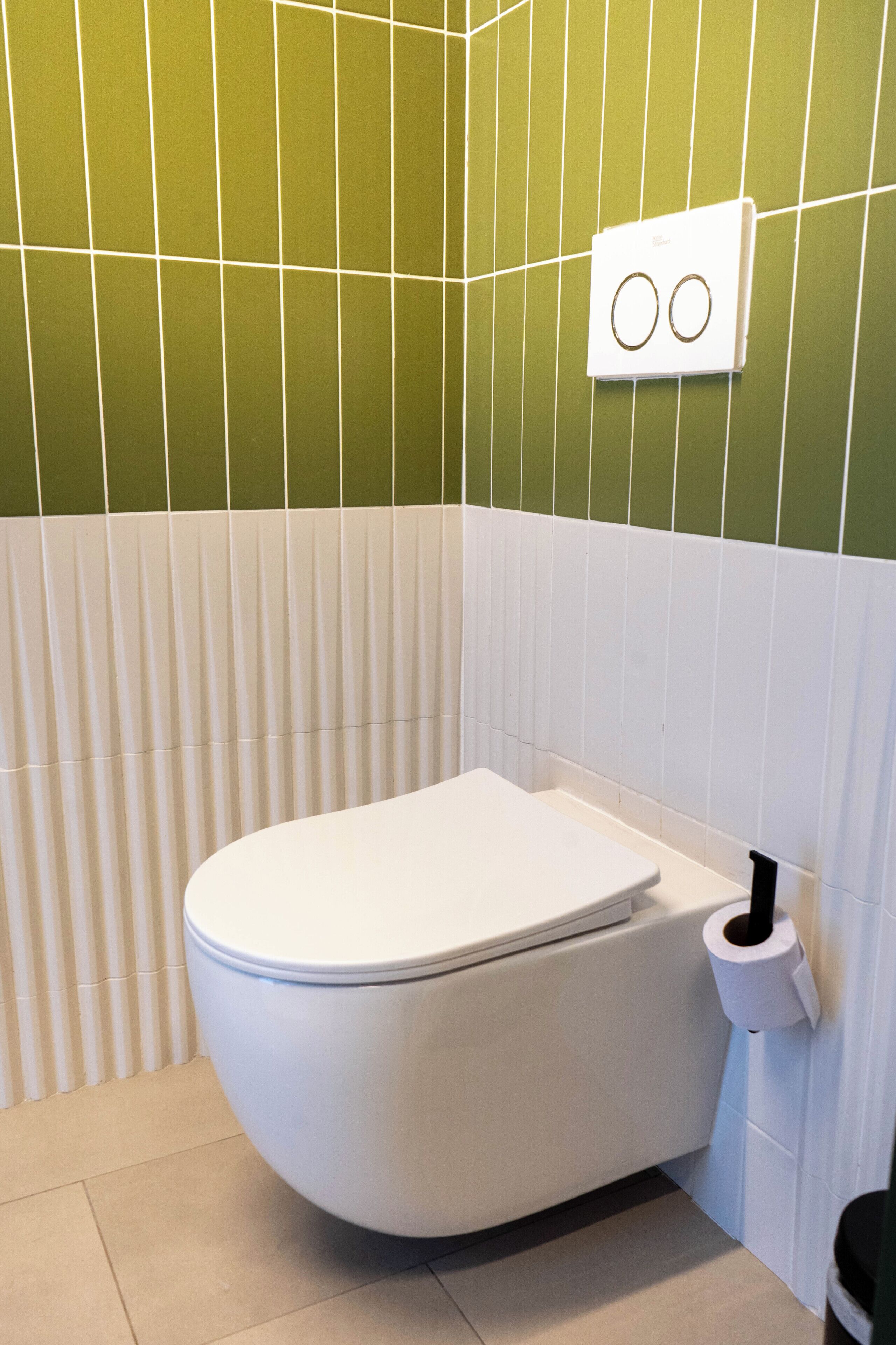 A bathroom with a white toilet, a white toilet paper holder, and green and white tiled walls.